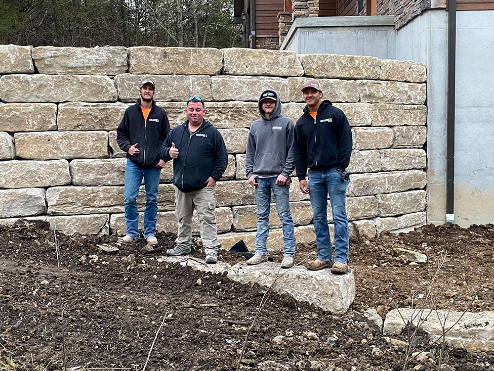 Gradex employees standing next to a stone retaining wall