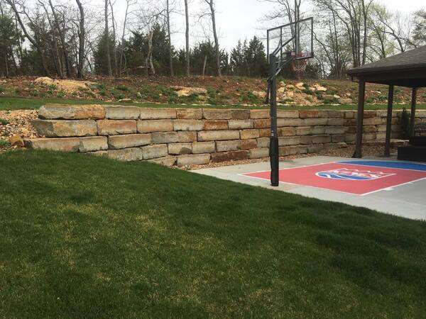 Retaining wall framing a seating area in a backyard with a half basketball court