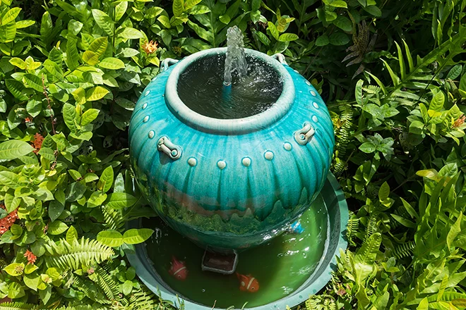 Small blue urn fountain in bushes